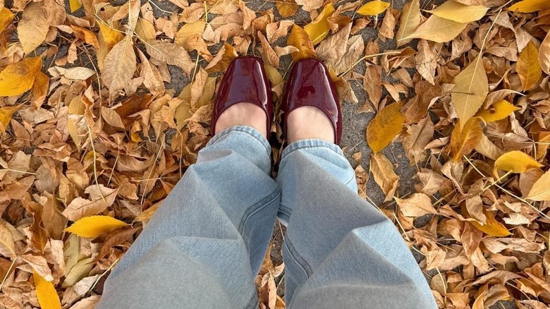 A woman wearing burgundy mary janes in fallen leaves