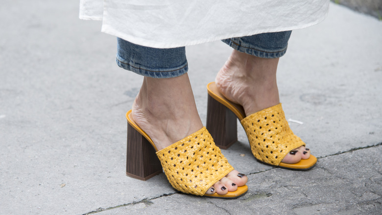 Close-up of woven mules in a bright yellow color worn on a city sidewalk