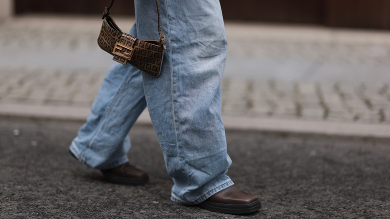 Close-up on baggy jeans being worn with brown shoes and skinny, brown handbag