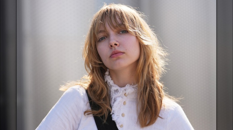 A woman posing in a white shirt with a neutral expression and full bangs