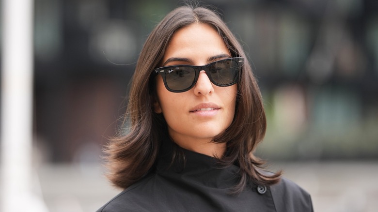 A woman with a neutral expression wearing sunglasses with a flippy lob haircut