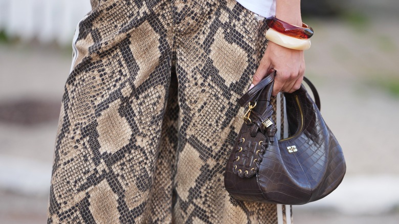 A woman's hand holding a croc-print brown hobo bag