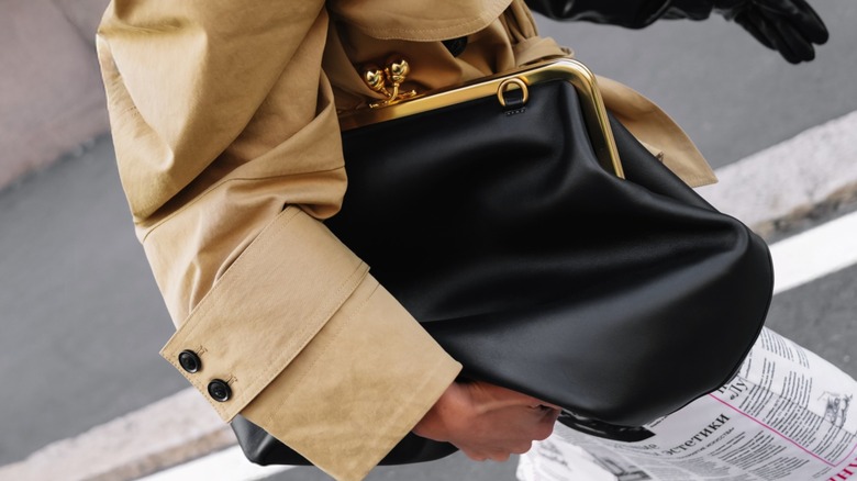A woman carrying a black kisslock bag under her arm
