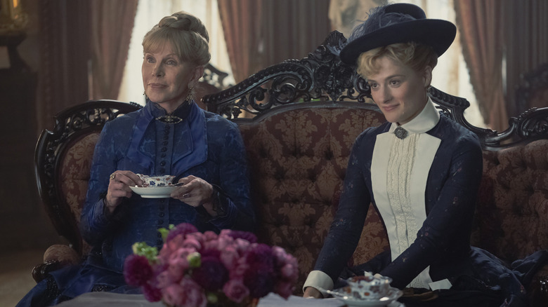 Two women in 1880-style clothing sitting on a ornate couch