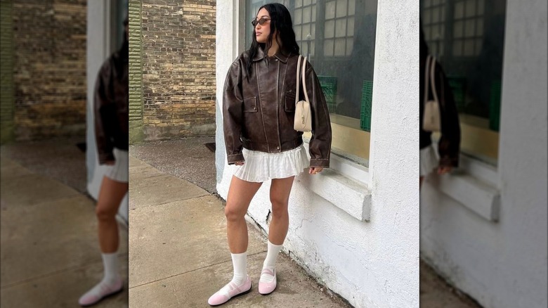 A woman in a leather coat with a white skirt and pink ballet sneakers