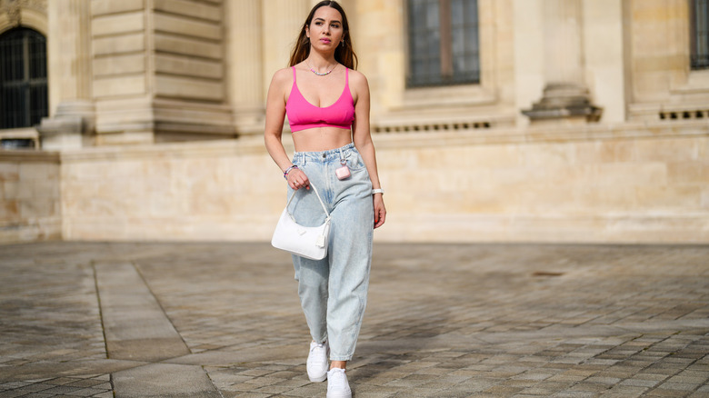 A woman walking in a pink bralette with jeans and white sneakers