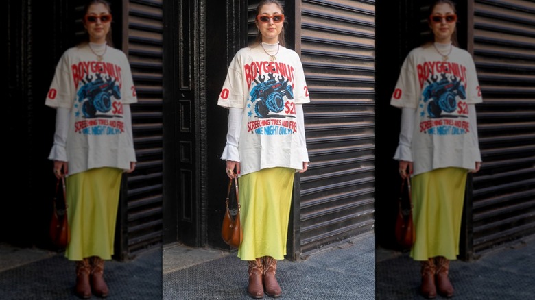 A woman standing on the street in a yellow midi skirt, oversized t-shirt, and cowboy boots