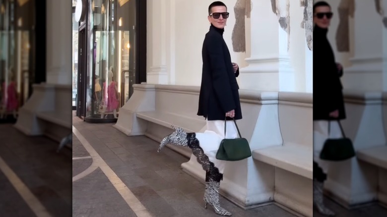 A woman posing on the street in a white slip skirt, blazer, and zebra print boots