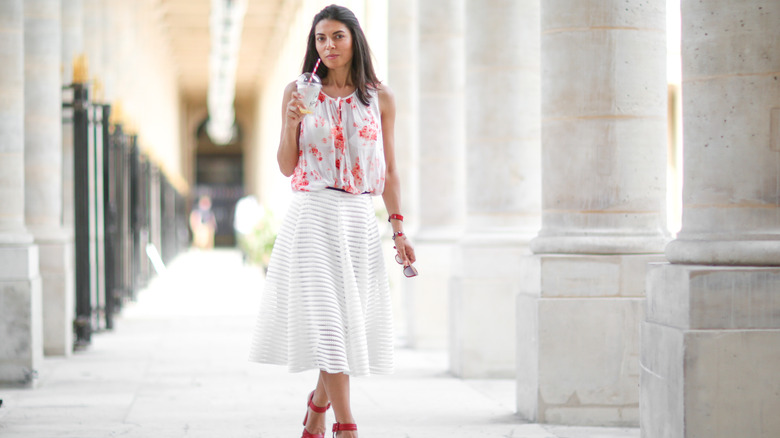 A woman in a white skirt sipping a drink