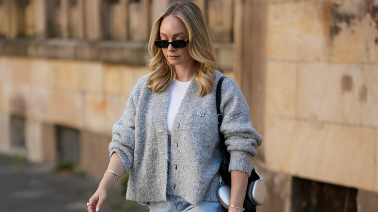 Blond fashion week guest wearing a sizable, grey cardigan over a simple white shirt