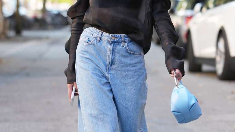 Woman wearing jeans and carrying a purse and phone
