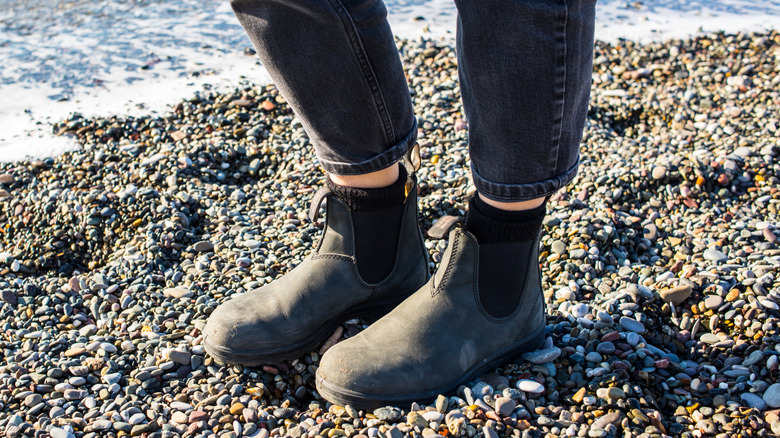 Person standing on a pebbled beach in gray Blundstone's