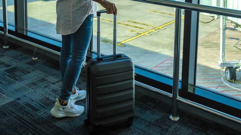 Woman walking through an airport terminal with black rolling luggage and sneakers