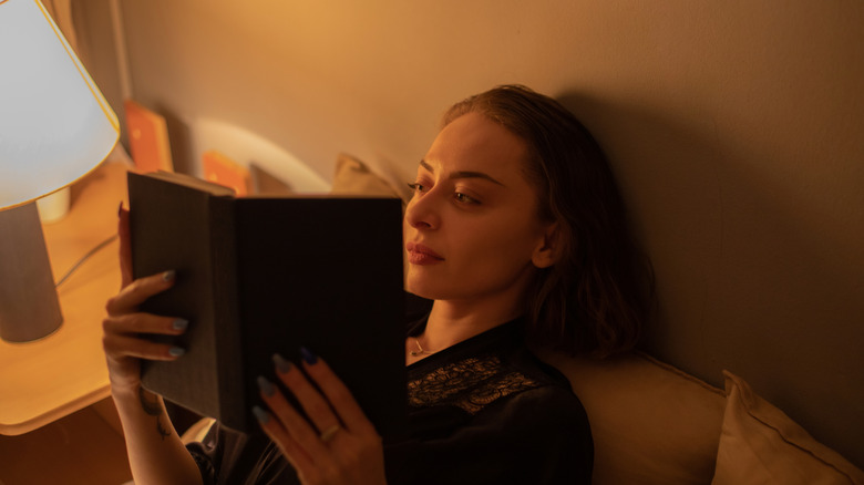 Young woman relaxing in bed reading a book at night