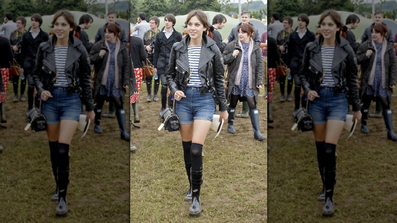 Alexa Chung walks wearing knee-high black socks, a leather jacket, and denim mini-shorts