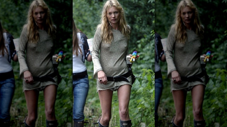 Kate Moss walks wearing a gold dress with a black belt and Hunter wellies