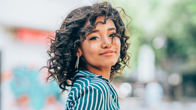 Woman with shorter curly hair looking toward the camera smirking