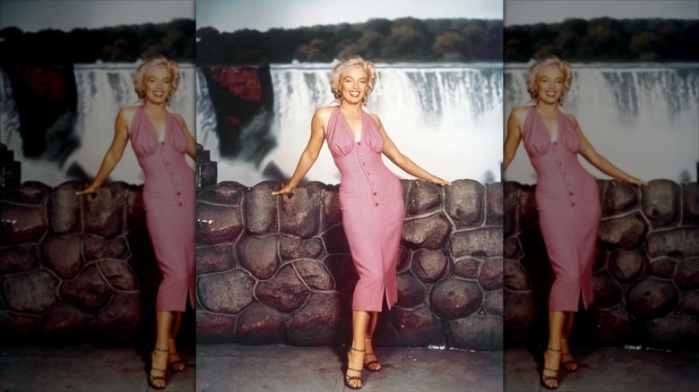 Marilyn Monroe wearing a pink button-down dress and strappy heels.