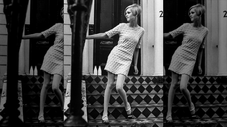 Twiggy holds onto a handrail wearing a white minidress