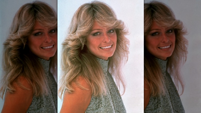 Farrah Fawcett looking to the side and into the camera with her hair styled in feathered layers and middle-parted bangs