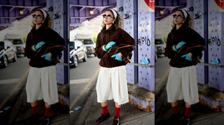 A NYFW attendee poses for a photo in a brown suede jacket paired with wide leg pants and red statement socks