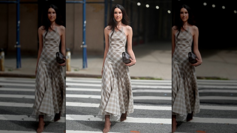 Danielle Smith is seen wearing a Kallmeyer beige and white plaid halter neck maxi dress, brown pointed toe boots and holding a brown clutch bag outside of the Kallmeyer show, during New York Fashion Week
