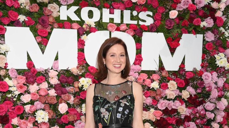 Ellie Kemper smiling under a Kohl's Mom sign in 2025