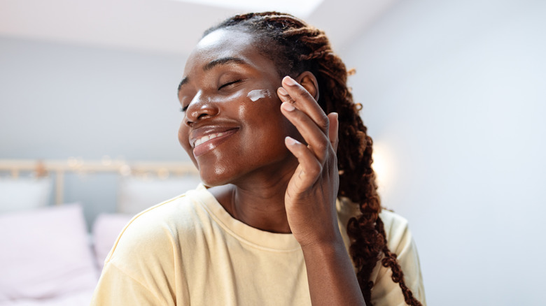 A woman applying lotion to her face