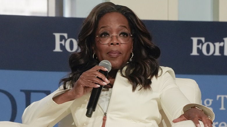 Oprah Winfrey, dressed in white and speaking into a microphone during an event