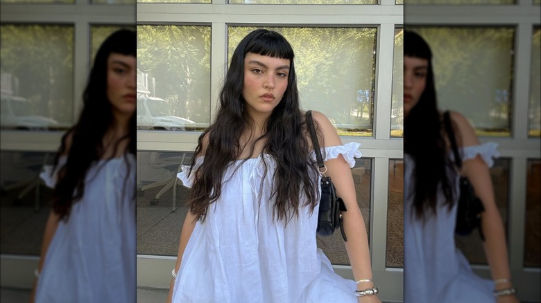 A woman wearing a white nightgown with long dark hair with blunt baby bangs
