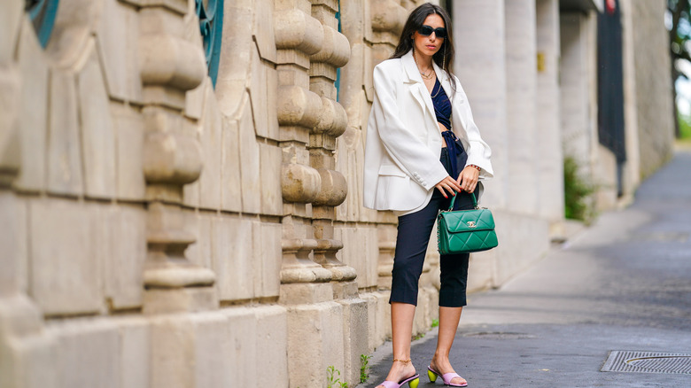 A woman standing in capris, a white blazer, and a green handbag
