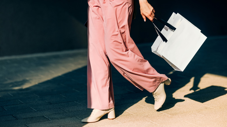 A woman in pink pants and heel walking and carrying shopping bags