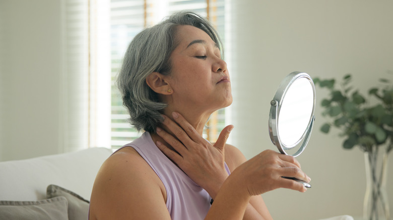 A young woman in a pink bathrobe examining her face in the mirror