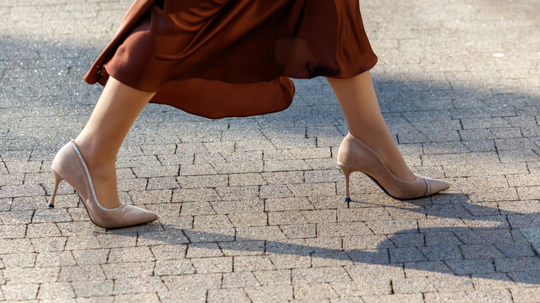 A close up of a woman wearing pink hue nude heels and walking on the street