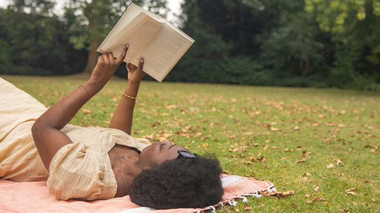Woman laying on blanket outdoors, reading raised book