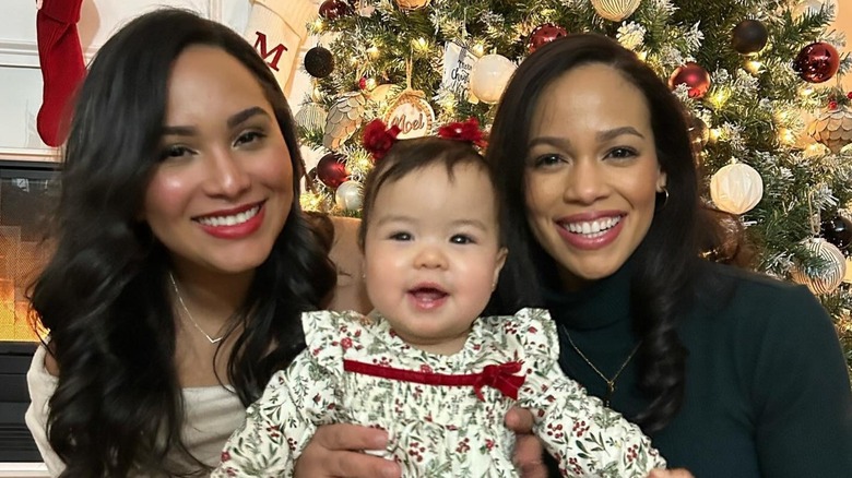 Juani Feliz and Claribel Jimenez-Feliz posing with their daughter in front of a Christmas tree