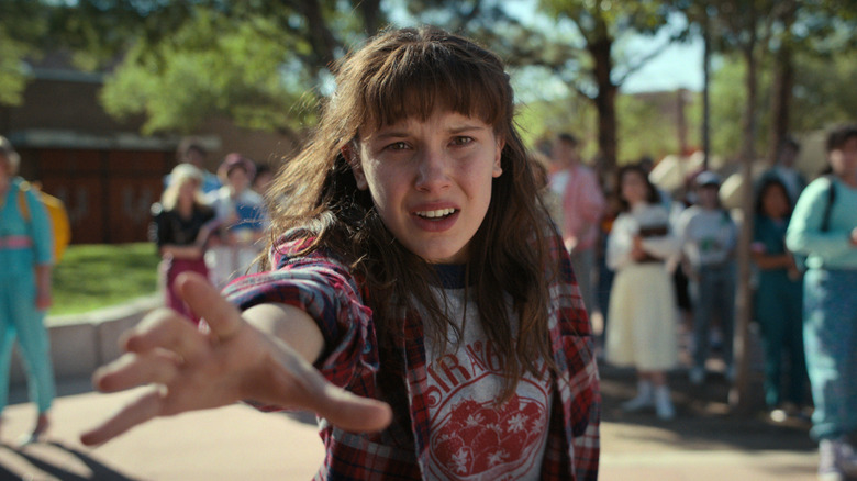 Millie Bobby Brown as Eleven in "Stranger Things" with long hair and her hand outstretched