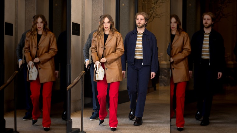 Maya Hawke wearing red pants and walking next to boyfriend Christian Lee Hutson