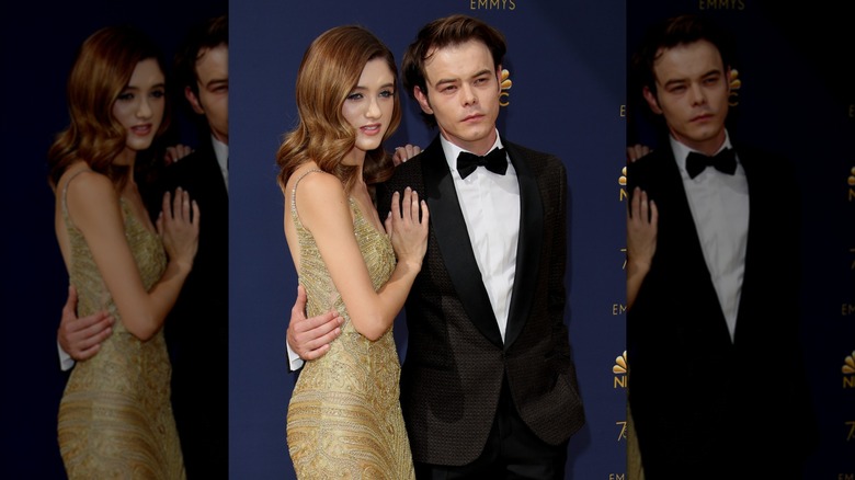 Natalia Dyer wearing a gold dress and standing next to Charlie Heaton who is wearing a tuxedo