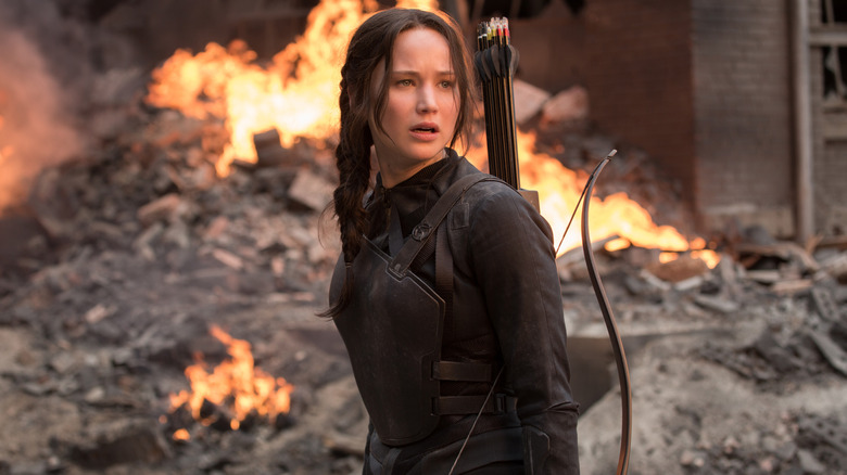 A film still of Jennifer Lawrence as Katniss holdling her bow and fire behind here