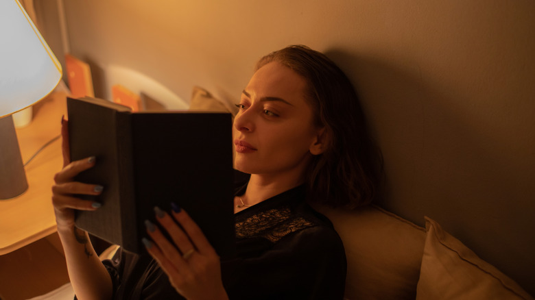 A woman wraps herself in a blanket and reads a book