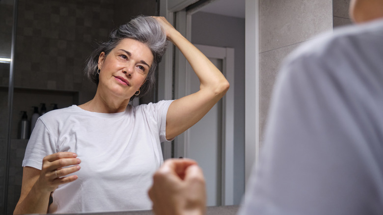 Mature woman taking care of her gray hair, styling it in front of the bathroom mirror during her morning routine