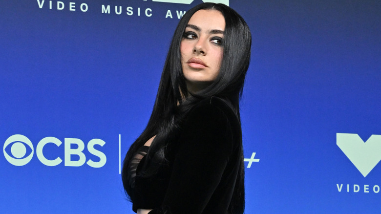 Charli XCX looking over her shoulder while wearing a black outfit and smokey eye on the MTV VMA red carpet
