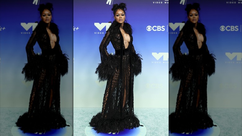 Teyana Taylor standing with her hand on her hips while wearing a deep-cut coat dress