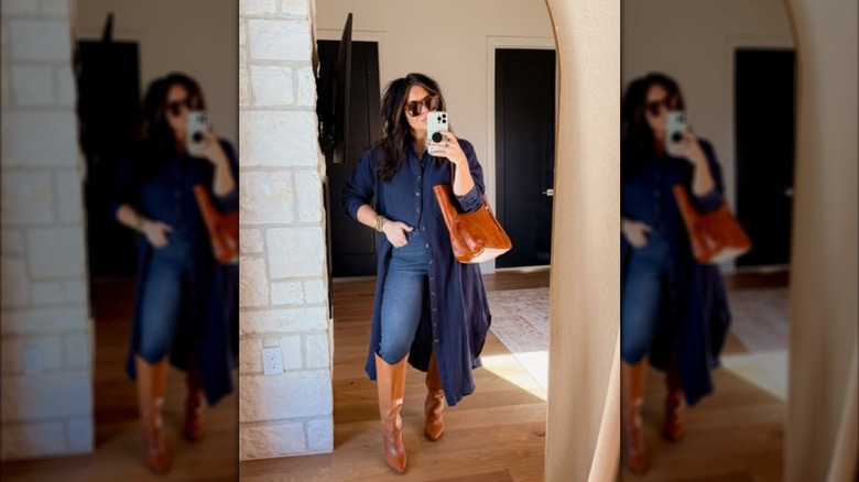 A woman takes her photo in mirror while wearing tall boots over jeans