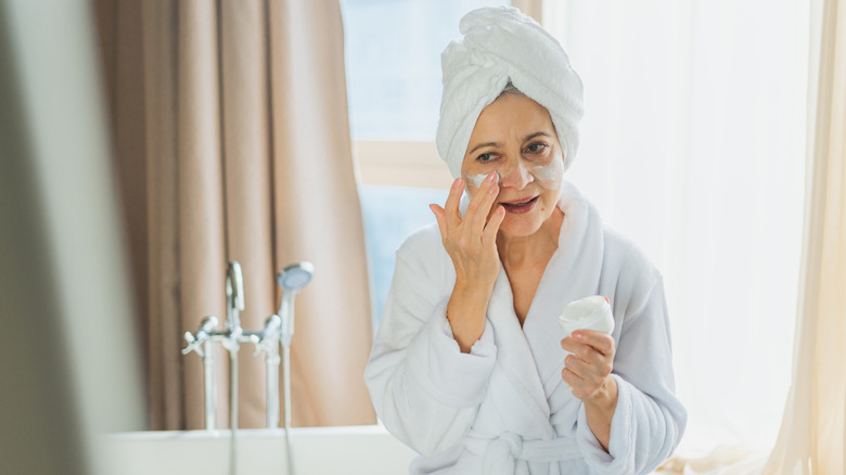 An older woman applying face cream while looking at the mirror