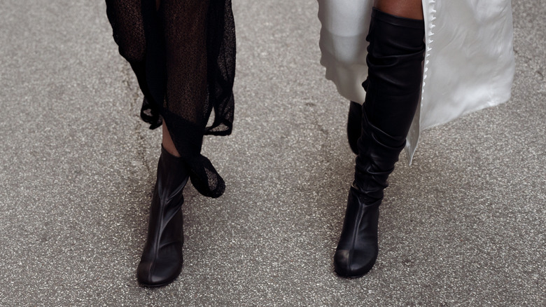 Close-up of unseen women wearing different-height boots and skirts while walking on pavement