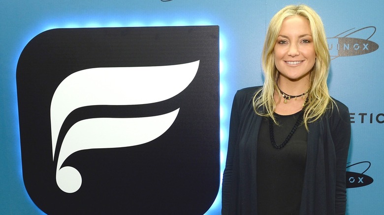 Kate Hudson smiling next to the Fabletics logo in 2013