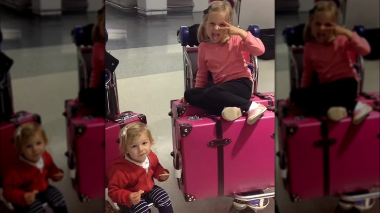 Two little girls, Cosima and Romy Mars, sitting on a stack of pink luggage