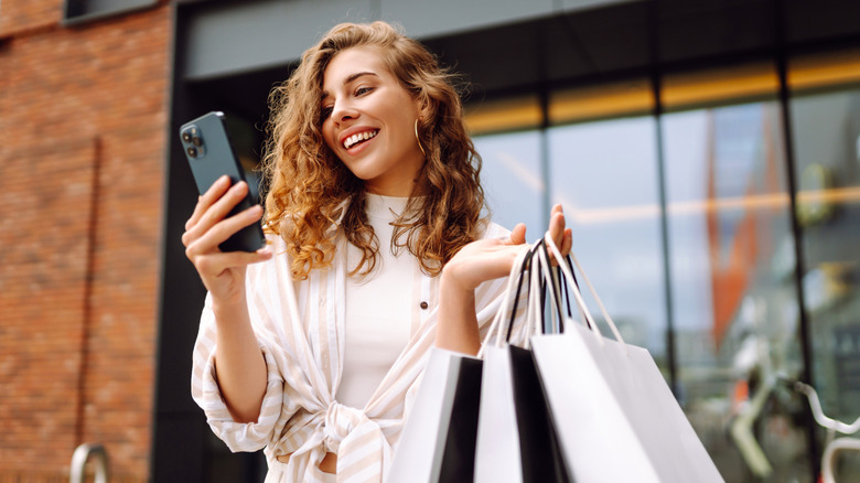 A woman holding shopping bags and looking at her phone